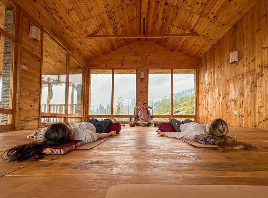 Two women practicing a sound bath in a timber hut with an instructor