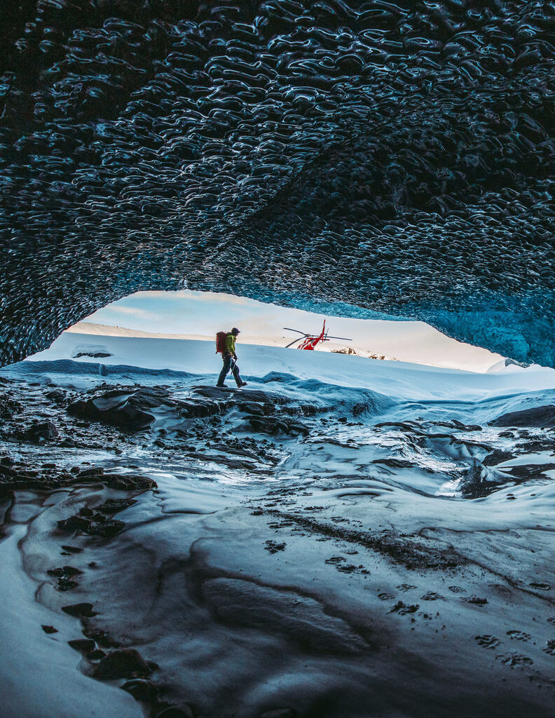 Shot from within an ice cave of hiker with helicopter in background