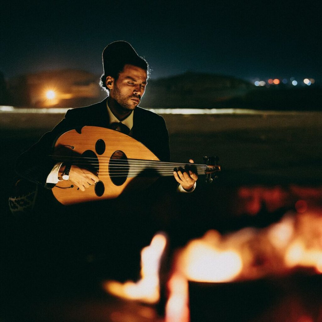 Musician playing Oud besides a fire at night