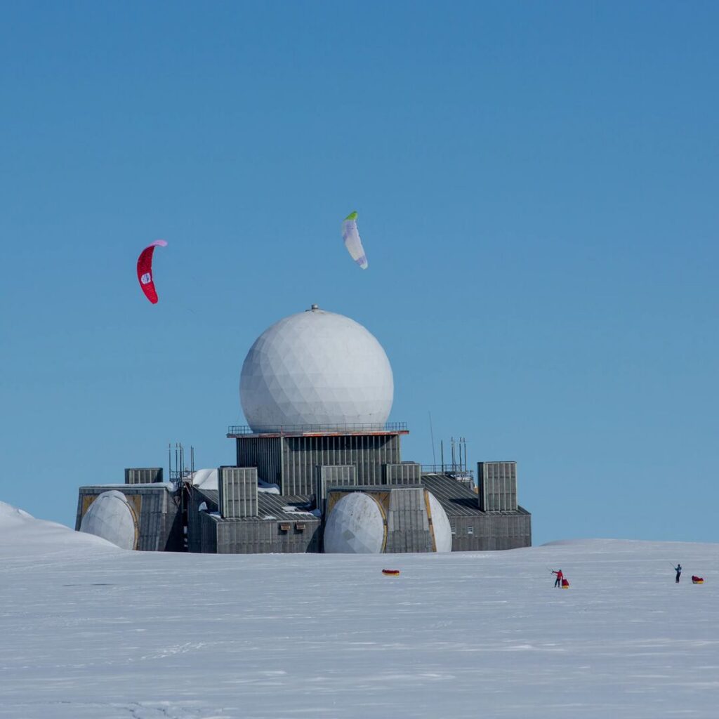 Two kite skiers travel past abandoned radar station in Greenland